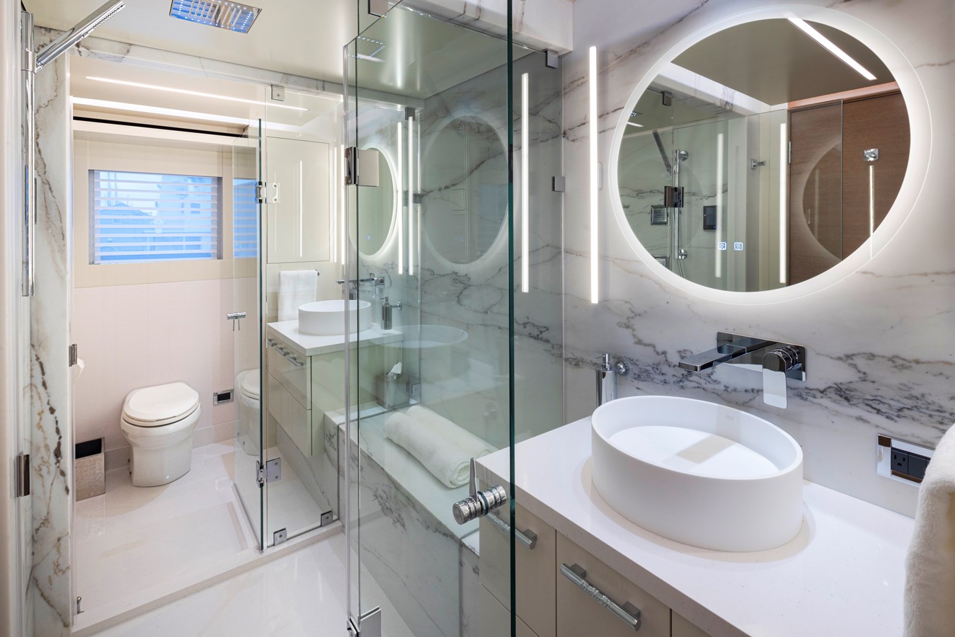 Westport W117 master bathroom with marble walls, glass shower, and round LED mirror